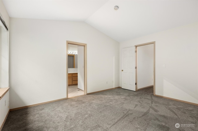 unfurnished bedroom featuring ensuite bath, lofted ceiling, baseboards, and light carpet