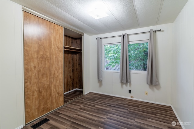 unfurnished bedroom with a closet, dark hardwood / wood-style floors, wooden walls, and a textured ceiling