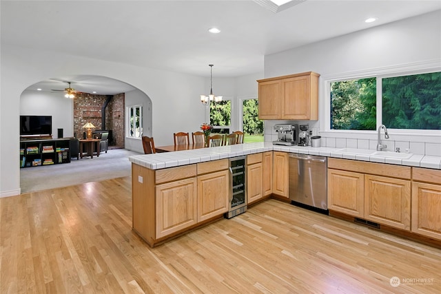 kitchen with dishwasher, sink, a wood stove, kitchen peninsula, and a healthy amount of sunlight