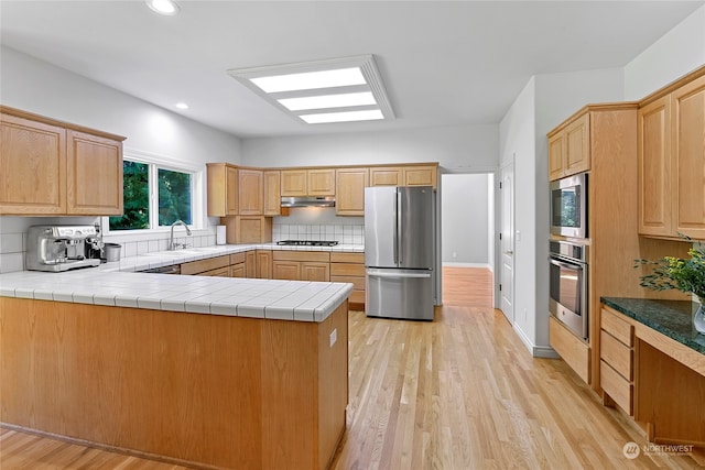 kitchen featuring light hardwood / wood-style floors, tile counters, kitchen peninsula, backsplash, and appliances with stainless steel finishes