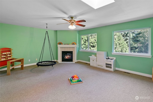 game room featuring ceiling fan, carpet, and a tile fireplace