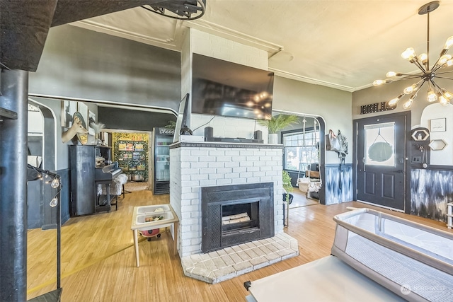 living room with a notable chandelier, a brick fireplace, ornamental molding, and hardwood / wood-style flooring