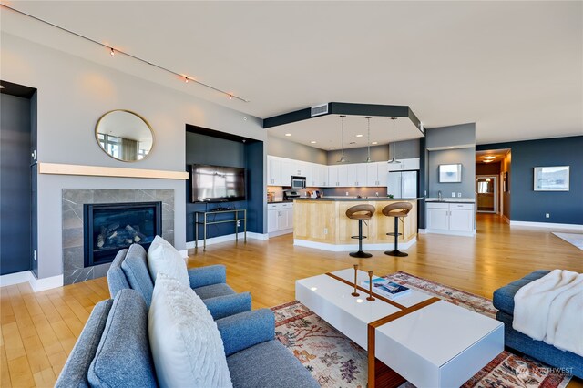 living room featuring rail lighting, light hardwood / wood-style flooring, and a tile fireplace