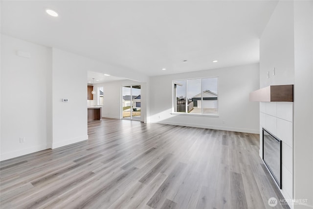 unfurnished living room with light wood-type flooring and a tiled fireplace