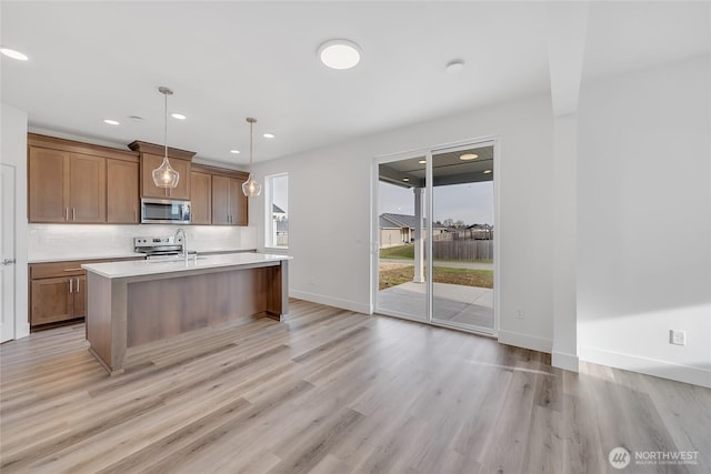 kitchen featuring a center island with sink, light hardwood / wood-style flooring, appliances with stainless steel finishes, decorative backsplash, and pendant lighting