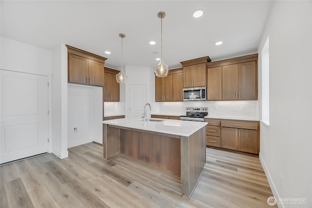 kitchen with a center island with sink, sink, light wood-type flooring, decorative light fixtures, and stainless steel appliances