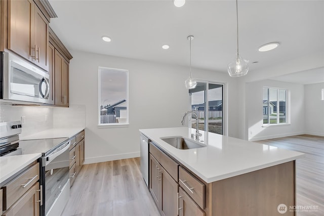 kitchen featuring a center island with sink, appliances with stainless steel finishes, sink, backsplash, and decorative light fixtures