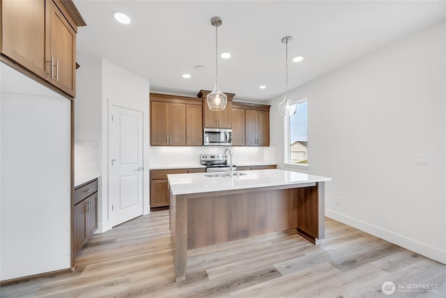 kitchen featuring appliances with stainless steel finishes, light hardwood / wood-style flooring, sink, and pendant lighting