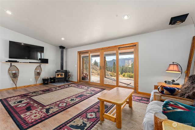 living room featuring light hardwood / wood-style flooring, vaulted ceiling, and a wood stove