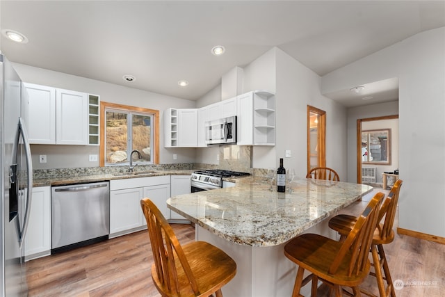 kitchen with light stone counters, stainless steel appliances, kitchen peninsula, white cabinetry, and vaulted ceiling