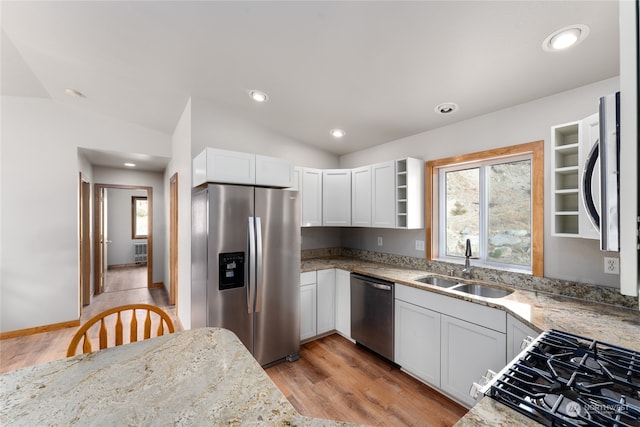 kitchen featuring sink, light hardwood / wood-style flooring, white cabinetry, stainless steel appliances, and vaulted ceiling