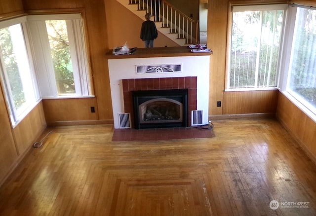 unfurnished living room with a fireplace, wooden walls, and a healthy amount of sunlight