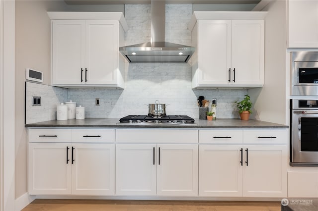 kitchen featuring stainless steel appliances, wall chimney exhaust hood, white cabinetry, and decorative backsplash