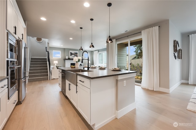 kitchen with sink, a center island with sink, stainless steel appliances, and white cabinetry