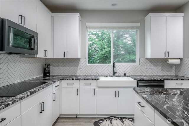 kitchen with dark stone counters, light hardwood / wood-style flooring, sink, stainless steel appliances, and white cabinetry