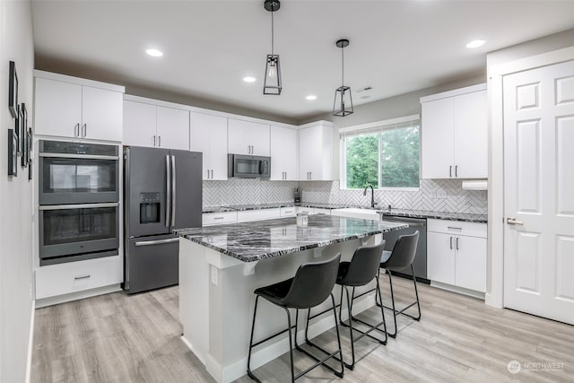 kitchen with a kitchen island, light hardwood / wood-style flooring, decorative light fixtures, white cabinetry, and appliances with stainless steel finishes