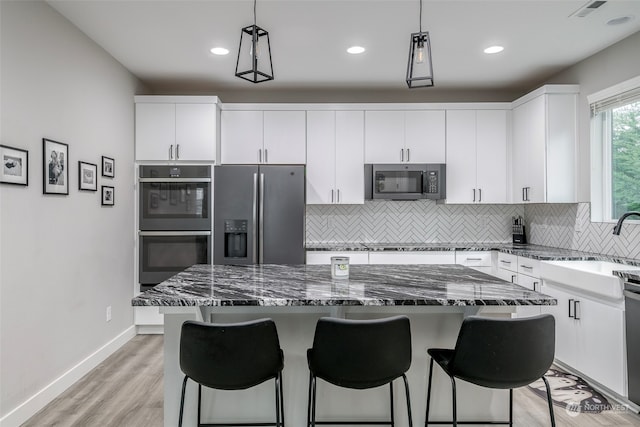 kitchen with stainless steel appliances, pendant lighting, a kitchen island, and white cabinetry