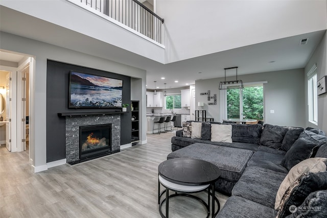 living room featuring a fireplace, plenty of natural light, a towering ceiling, and light hardwood / wood-style flooring