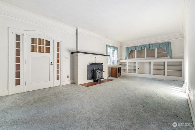 unfurnished living room featuring a wood stove, crown molding, and carpet flooring