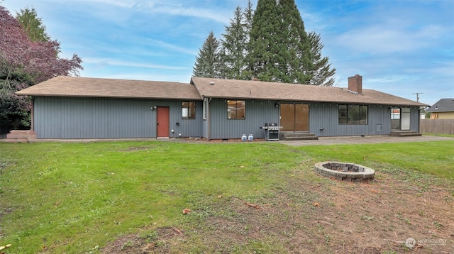 rear view of house with an outdoor fire pit and a yard