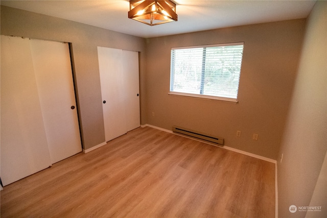 unfurnished bedroom featuring light wood-type flooring and baseboard heating