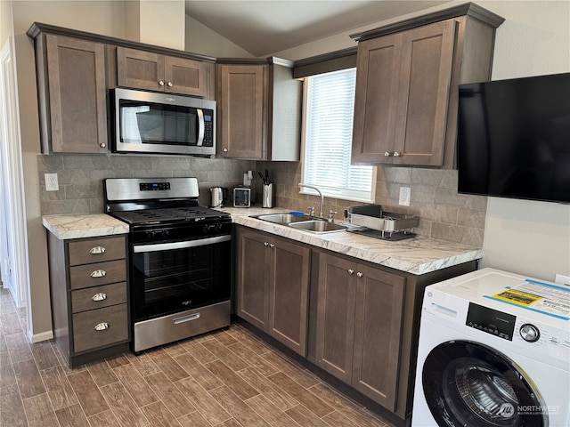 kitchen with lofted ceiling, sink, stainless steel appliances, dark brown cabinetry, and washer / dryer