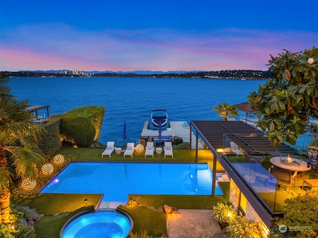 pool at dusk with a water view, a lawn, and an in ground hot tub