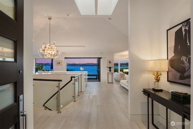 hallway with a chandelier, light hardwood / wood-style floors, and high vaulted ceiling