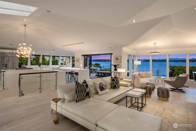 living room featuring a water view, a notable chandelier, lofted ceiling, and light wood-type flooring