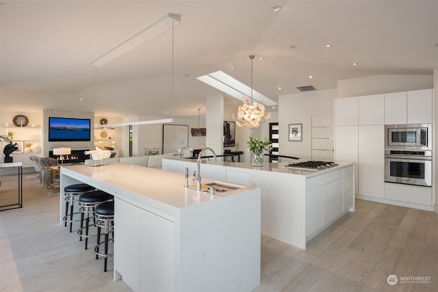 kitchen with a large island with sink, hanging light fixtures, stainless steel appliances, and white cabinetry