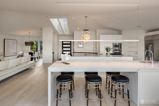 kitchen with a large island with sink, pendant lighting, sink, and white cabinets