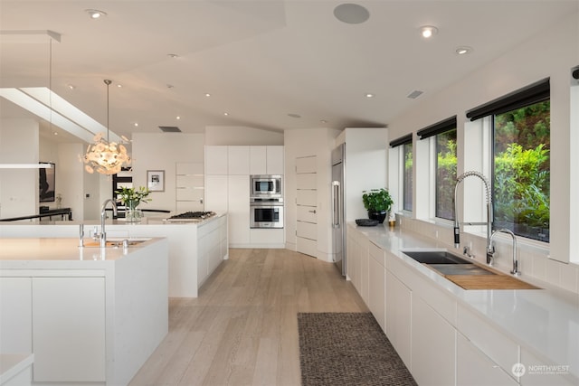 kitchen featuring white cabinets, sink, decorative light fixtures, stainless steel appliances, and light wood-type flooring