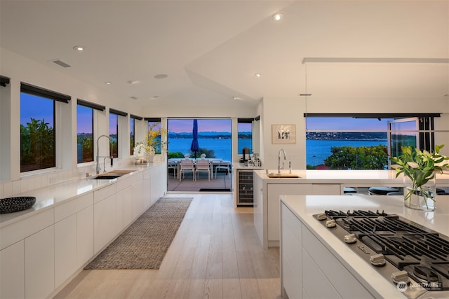 kitchen featuring a water view, light wood-type flooring, beverage cooler, sink, and white cabinets