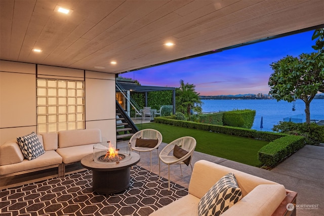 patio terrace at dusk featuring an outdoor living space with a fire pit, a yard, and a water view