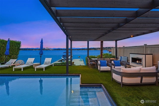 pool at dusk with a pergola, outdoor lounge area, a patio area, a lawn, and a water view