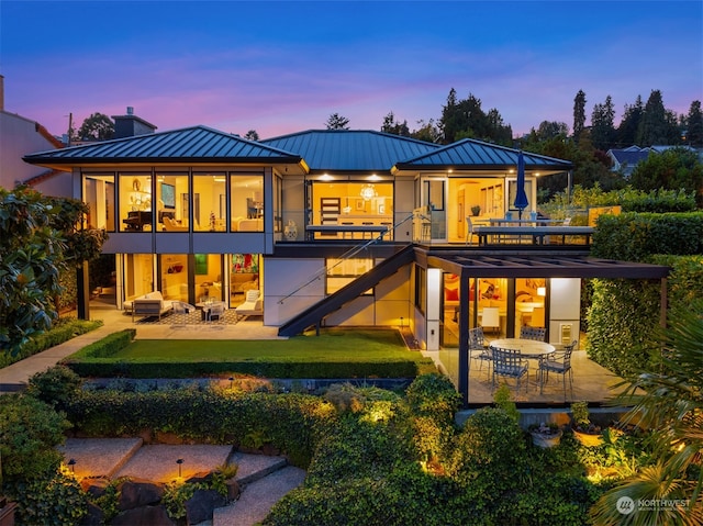 back house at dusk featuring a balcony and a patio area