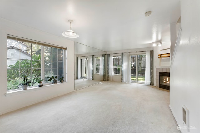 unfurnished living room featuring light carpet, a healthy amount of sunlight, and a tile fireplace