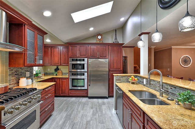 kitchen featuring appliances with stainless steel finishes, sink, hanging light fixtures, wall chimney exhaust hood, and decorative backsplash