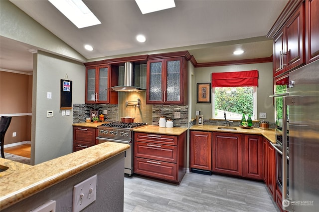 kitchen with wall chimney range hood, crown molding, lofted ceiling with skylight, appliances with stainless steel finishes, and light hardwood / wood-style floors