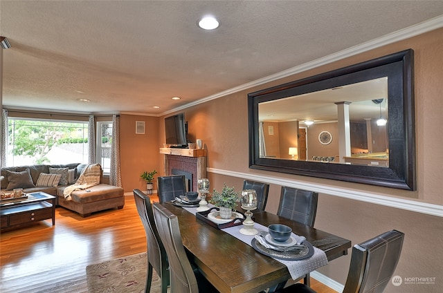 dining area featuring crown molding, a textured ceiling, a tiled fireplace, and wood-type flooring