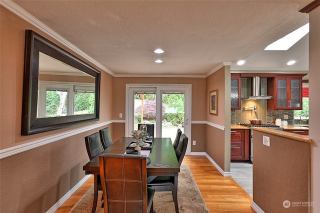 dining space with ornamental molding, a skylight, a textured ceiling, and light wood-type flooring