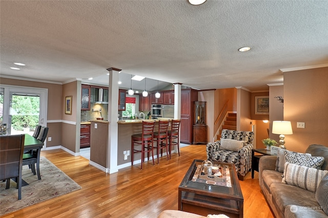 living room featuring decorative columns, light hardwood / wood-style flooring, a textured ceiling, and crown molding