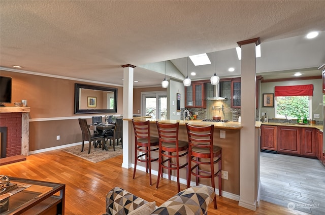 kitchen featuring a textured ceiling, light hardwood / wood-style floors, pendant lighting, ornamental molding, and a breakfast bar area