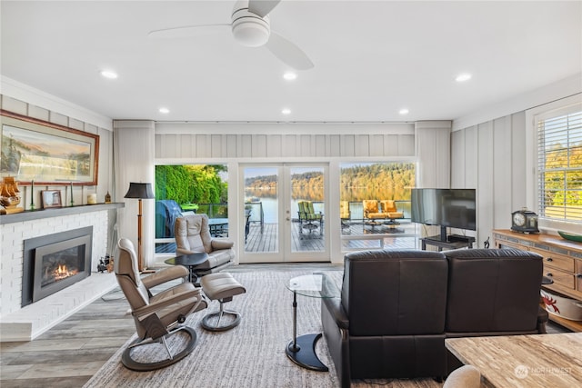 living room with french doors, a fireplace, crown molding, light wood-type flooring, and ceiling fan