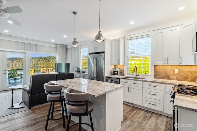 kitchen with stainless steel appliances, hardwood / wood-style floors, a kitchen island, white cabinetry, and decorative light fixtures