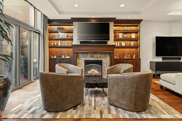 living area featuring built in features, a tray ceiling, a high end fireplace, and light hardwood / wood-style floors