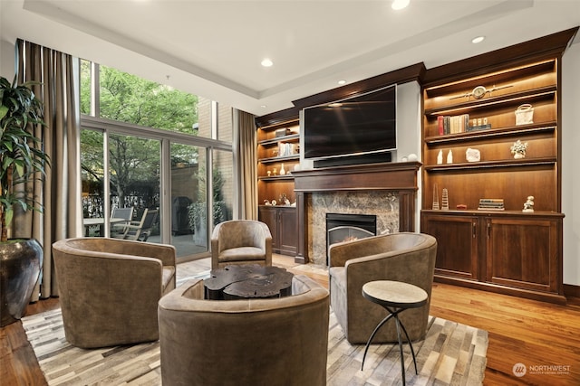 sitting room with built in features, a premium fireplace, and light wood-type flooring