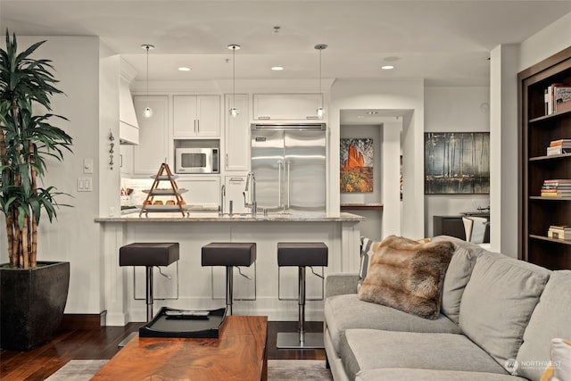 kitchen featuring built in appliances, kitchen peninsula, pendant lighting, light stone countertops, and white cabinets