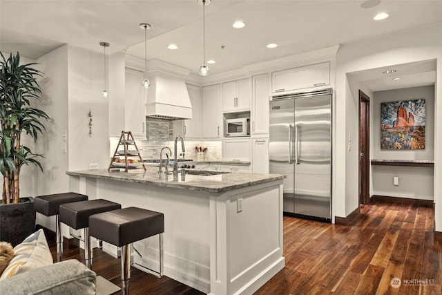 kitchen featuring pendant lighting, white cabinetry, stainless steel built in fridge, kitchen peninsula, and light stone countertops