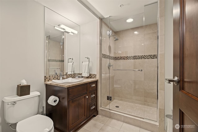 bathroom featuring tile patterned flooring, backsplash, vanity, a shower with shower door, and toilet